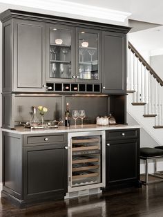 a kitchen with gray cabinets and wine glasses on the counter top, next to stairs