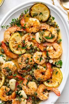 a white plate topped with shrimp, lemons and capers next to a glass of wine