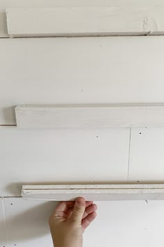 a hand is holding the edge of a white painted piece of wood on a wall