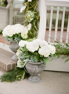 two vases filled with white flowers sitting on the side of a porch next to steps