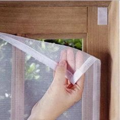 a hand is holding a piece of white paper in front of a window with sheer curtains