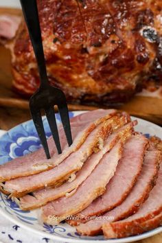 slices of ham on a blue and white plate with a fork sticking out of it