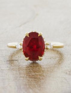 a close up of a ring with a red stone on it and two diamonds around the band