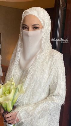 a woman dressed in white holding a bouquet of flowers and wearing a veil over her head