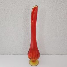 a red vase sitting on top of a white table next to a wall and floor