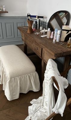 a wooden table topped with lots of clutter next to a white bench and mirror