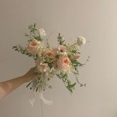 a bouquet of flowers being held by someone's hand in front of a white wall