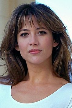 a close up of a person wearing a white shirt and looking at the camera with a serious look on her face