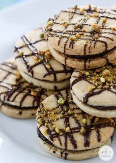 several cookies with chocolate drizzle and pistachio toppings on a white plate