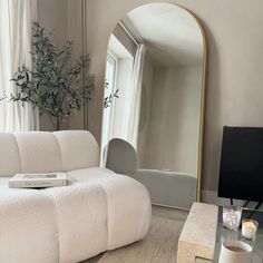 a living room with a couch, mirror and coffee table in front of the window