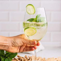 a hand holding a wine glass filled with water and lime