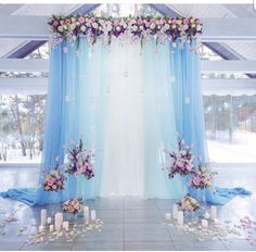 a blue and white wedding ceremony setup with flowers, candles and draping on the floor