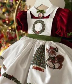 This charming vintage-inspired Christmas dress for girls features luxurious deep red velvet with puffy sleeves, perfect for capturing the holiday spirit. The dress is adorned with a beautiful detachable white apron, intricately embroidered with festive details including a Christmas wreath and a decorated tree. The green velvet waistband ties the look together, adding a touch of traditional holiday elegance. A small embroidered squirrel dressed in holiday attire sits by the tree, adding a playful and whimsical touch to the design. Ideal for holiday parties, family gatherings, or festive photo shoots, this timeless dress combines classic charm with modern holiday cheer. Crafted from premium velvet and cotton fabrics, your little one will feel both comfortable and regal during the holiday sea Embroidered Squirrel, Christmas Dress For Girls, Squirrel Dress, Deep Red Velvet, Velvet Embroidery, Vintage Inspired Christmas, Holiday Attire, White Apron, Timeless Dress