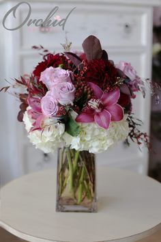 a vase filled with pink and white flowers on top of a wooden table next to a dresser