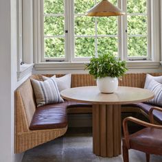 a corner table with two brown chairs and a white vase on it in front of a bay window