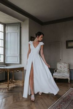 a woman in a white dress standing on a wooden floor next to a chair and rug