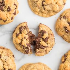 chocolate chip cookies are cut in half and placed on a marble counter top with one bite taken out