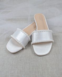 a pair of white slippers with pearls on the toes and heel are sitting on a bed