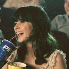 a man and woman sitting next to each other at a movie theater drinking from cups