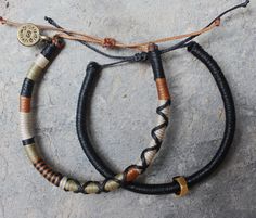 two bracelets with different colored cords and gold accents on top of a stone surface