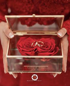 a woman holding a box with two wedding rings in it and red roses on the inside