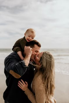 a man and woman holding a baby on the beach while they are kissing each other