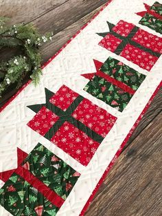 a quilted table runner with red and green christmas trees on it, next to a wreath