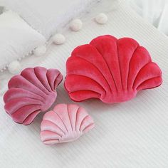 three pink and red scallop shaped pillows on a bed