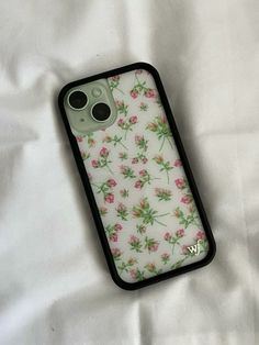 an iphone case with flowers on it laying on top of a white sheet covered bed