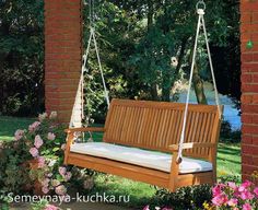 a wooden swing hanging from the side of a brick building next to flowers and trees