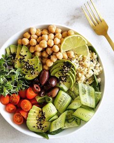 a white bowl filled with vegetables and chickpeas on top of a table next to a fork