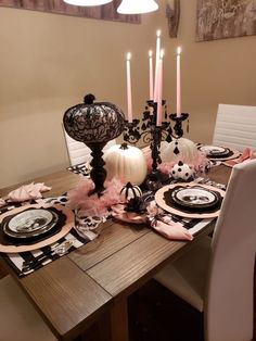 a dining room table set for halloween with black and white plates, candles and decorations