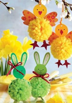 three paper rabbits are hanging from a branch with yellow flowers in the foreground and green pom - poms on the background