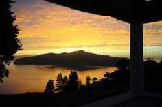 the sun is setting over a lake with mountains in the distance and trees around it