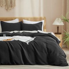 a bed covered in black and white linens next to a lamp on a wooden headboard