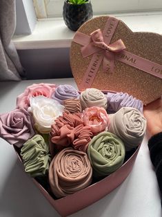 a pink heart shaped box filled with lots of different colored flowers next to a window