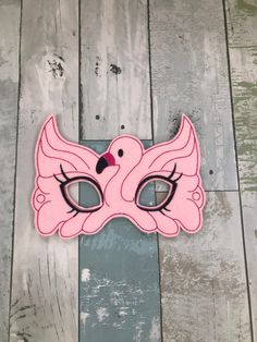 a pink mask with black eyes and a bird on the nose is sitting on a wooden floor