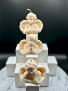 three small angel figurines sitting on top of a white stand with marble bases