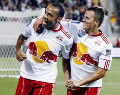 two men in red and white soccer uniforms standing next to each other on a field