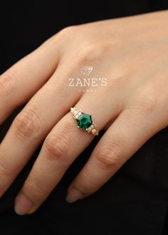 a woman's hand with an emerald and diamond ring on her left hand, wearing a black shirt