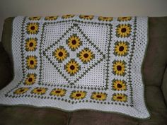 a crocheted blanket with sunflowers on it sitting on a couch next to a pillow