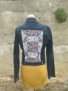 a denim jacket with colorful flowers on it and a yellow dress underneath the jean jacket