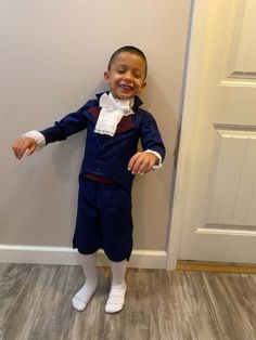 a young boy in a blue suit and white shirt standing next to a door with his hands on the wall