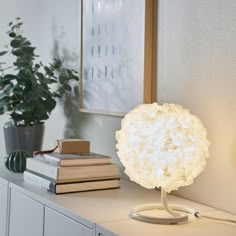 a white lamp sitting on top of a table next to some books and a potted plant