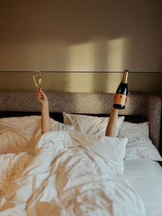 a person laying in bed with their feet up holding two wine glasses