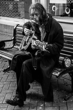 a man sitting on a bench playing an acoustic guitar