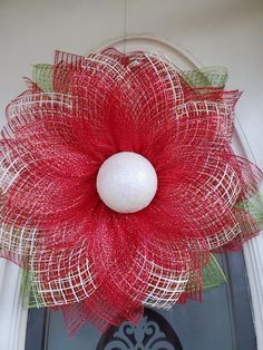 a red and white wreath on the front door with a ball hanging from it's center