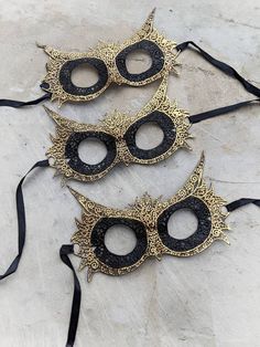 Wide-eyed and wise, owls perceive what other creatures do not, the perfect spirit to carry with you to a masquerade. This lace mask is stiffened and painted by hand in gold on the feathers and beak for extra intrigue. One size fits most. Ties with satin ribbon. Black Fantasy Costume Accessories As Gift, Black Halloween Masks As Gifts, Black Masks And Prosthetics For Carnival Gift, Gold Masks And Prosthetics For Carnival Festival, Black Masquerade Mask For Halloween Gift, Black Masks For Halloween Gift, Black Costume Accessories For Carnival Gift, Black Masks And Prosthetics For Carnival, Black Carnival Costume Accessories Gift