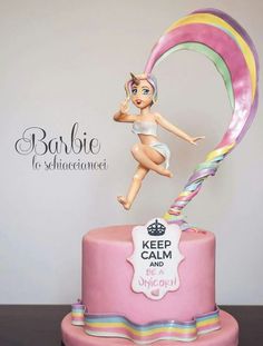 a pink cake with a barbie doll on top and a rainbow ribbon around the base