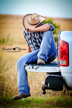 a man sitting on the back of a pickup truck in a field with his hat over his head